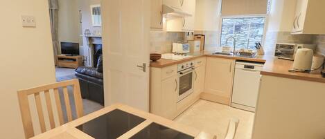 A modern kitchen with white cabinets, a built-in oven, a dishwasher, and a window providing natural light.