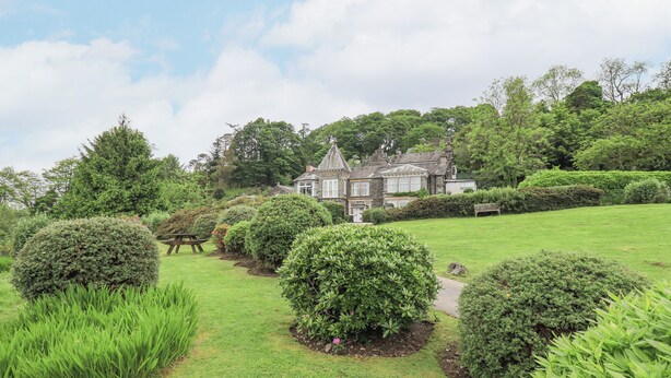 A large, historic house surrounded by well-maintained lawns and hedges.