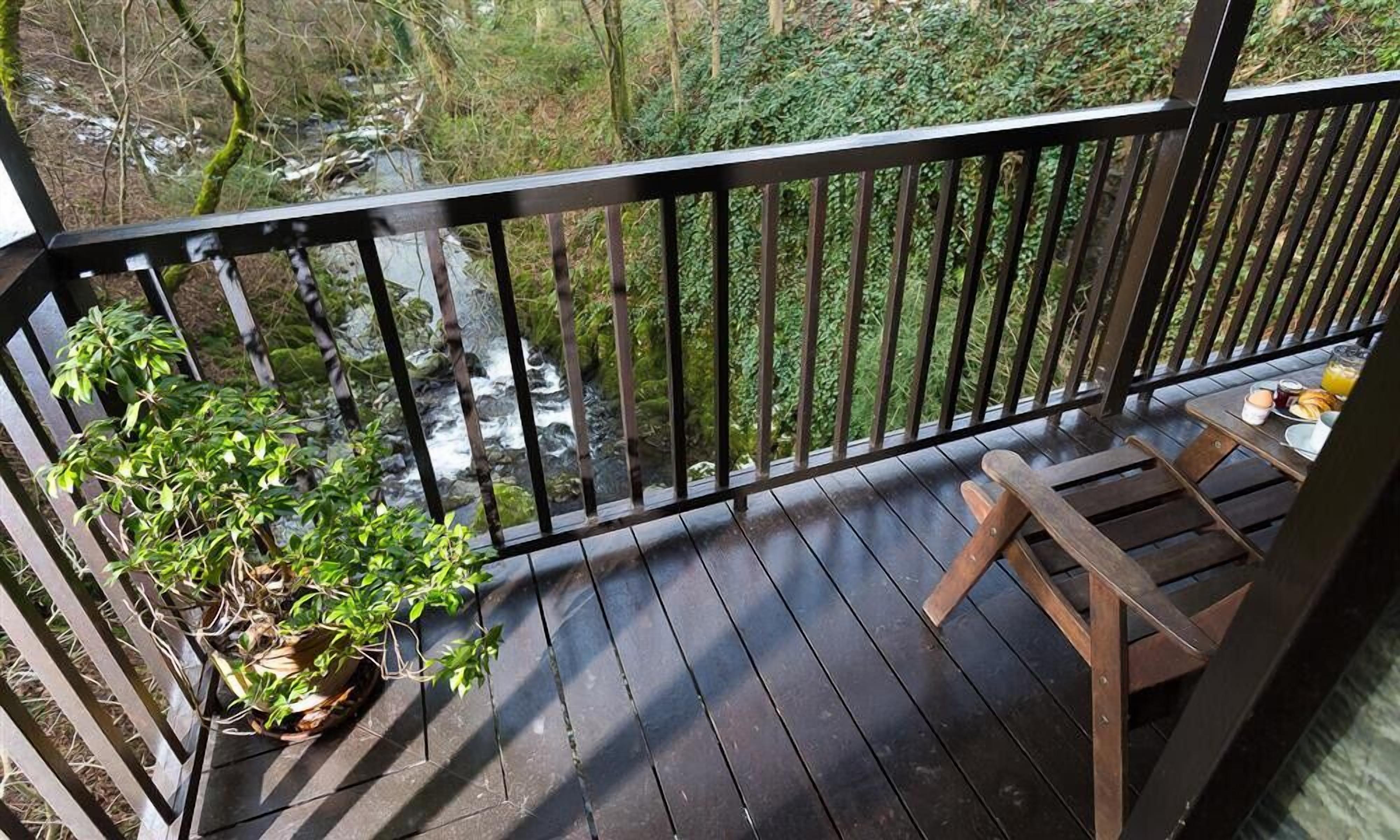 Um deck de madeira com guarda-corpo, uma mesa com itens de café da manhã e um vaso com planta.