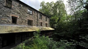 A stone building with a sloped roof, surrounded by dense greenery.