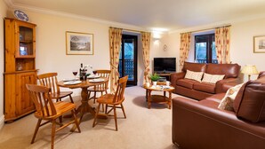 A living room with a brown leather sofa, wooden dining table with chairs, a television, and a cabinet.