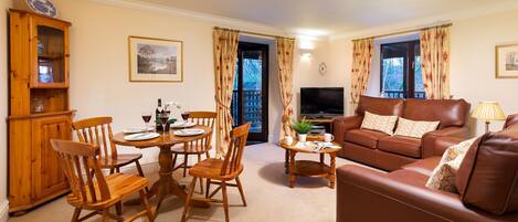 A living room with a brown leather sofa, wooden dining table with chairs, a television, and a cabinet.
