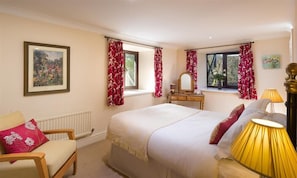 A bedroom with a large bed, a chair, a dresser, and two windows with curtains.