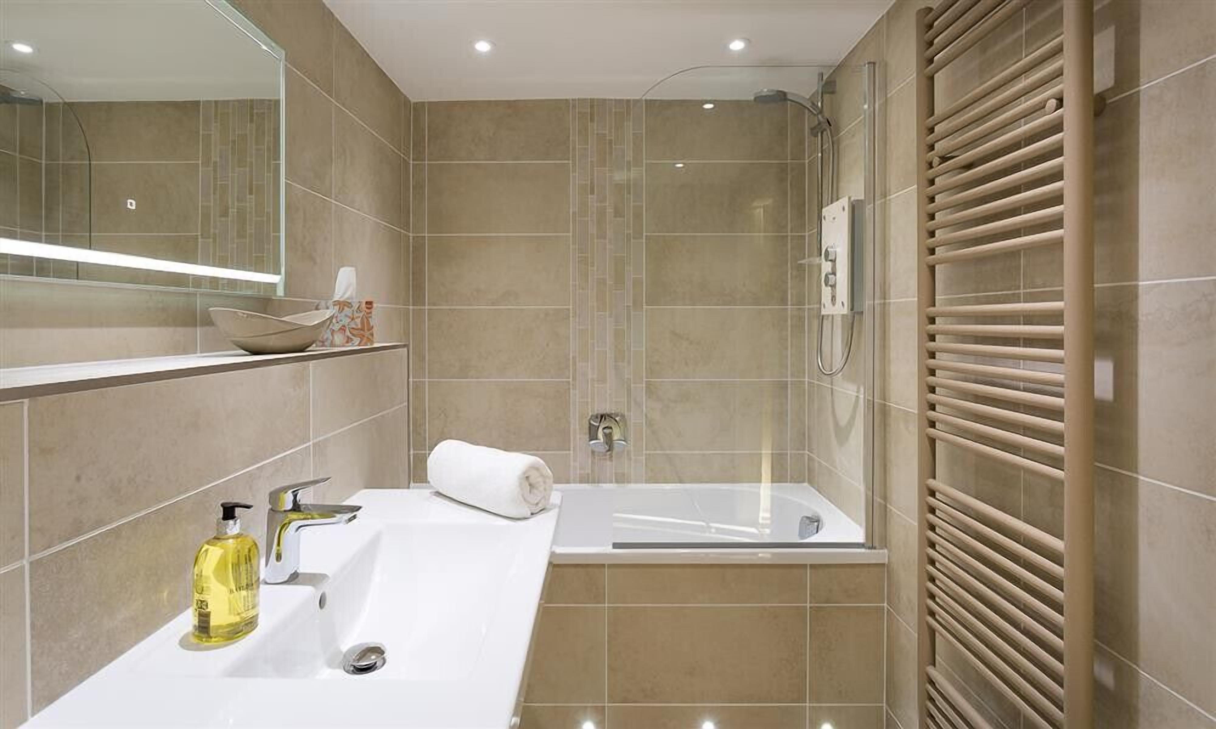 A modern bathroom with a large mirror, a sink, a bathtub, and a shower.
