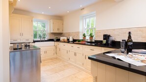 A modern kitchen with white cabinets, a black countertop, and a stainless steel range hood. - Grass Ings (Ambleside)