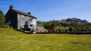 A stone house with a large window and a view of a hill. - Grass Ings (Ambleside)