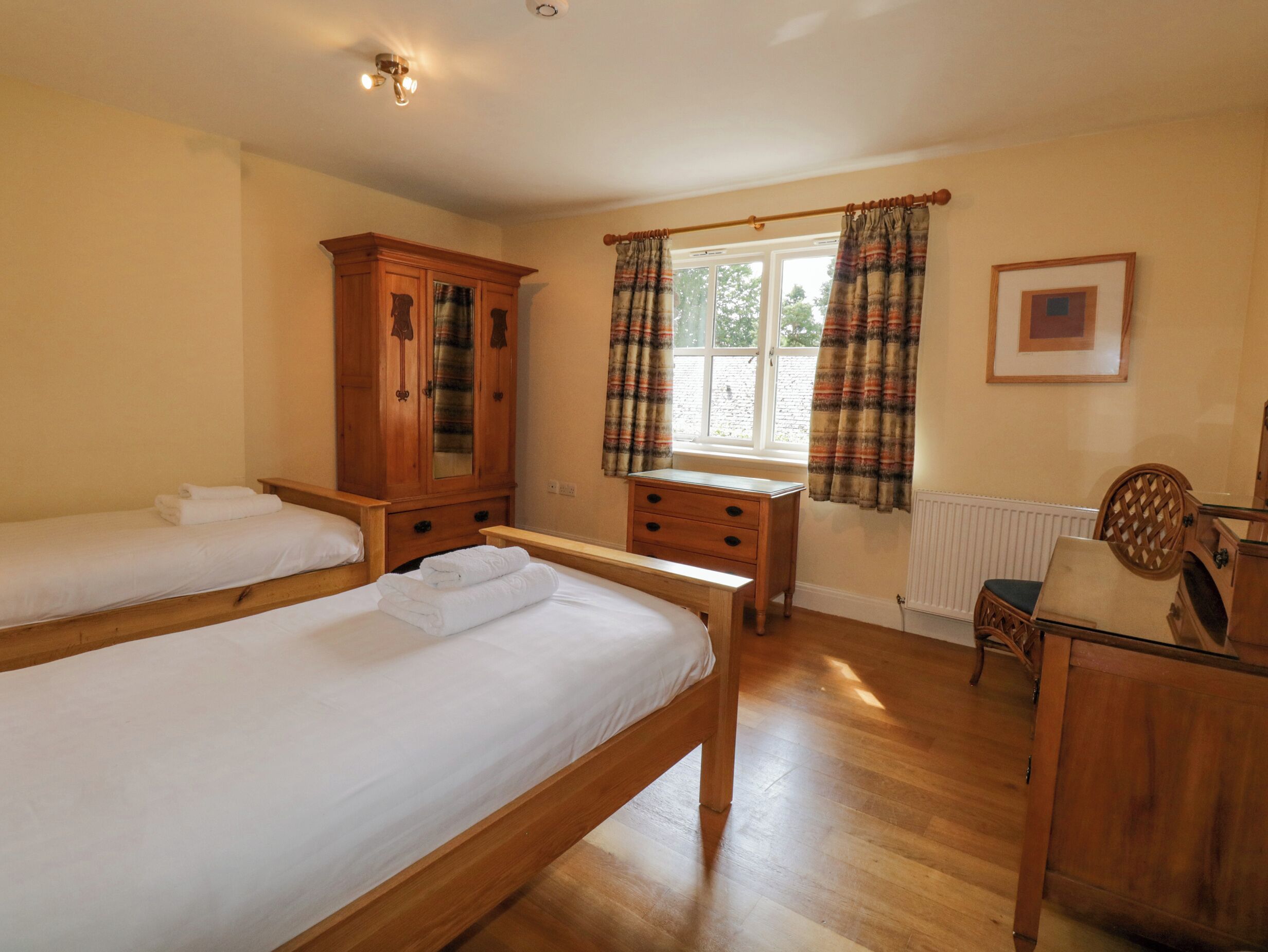 A room with two wooden beds, a wooden cabinet, a wooden chair, and a window with curtains.
