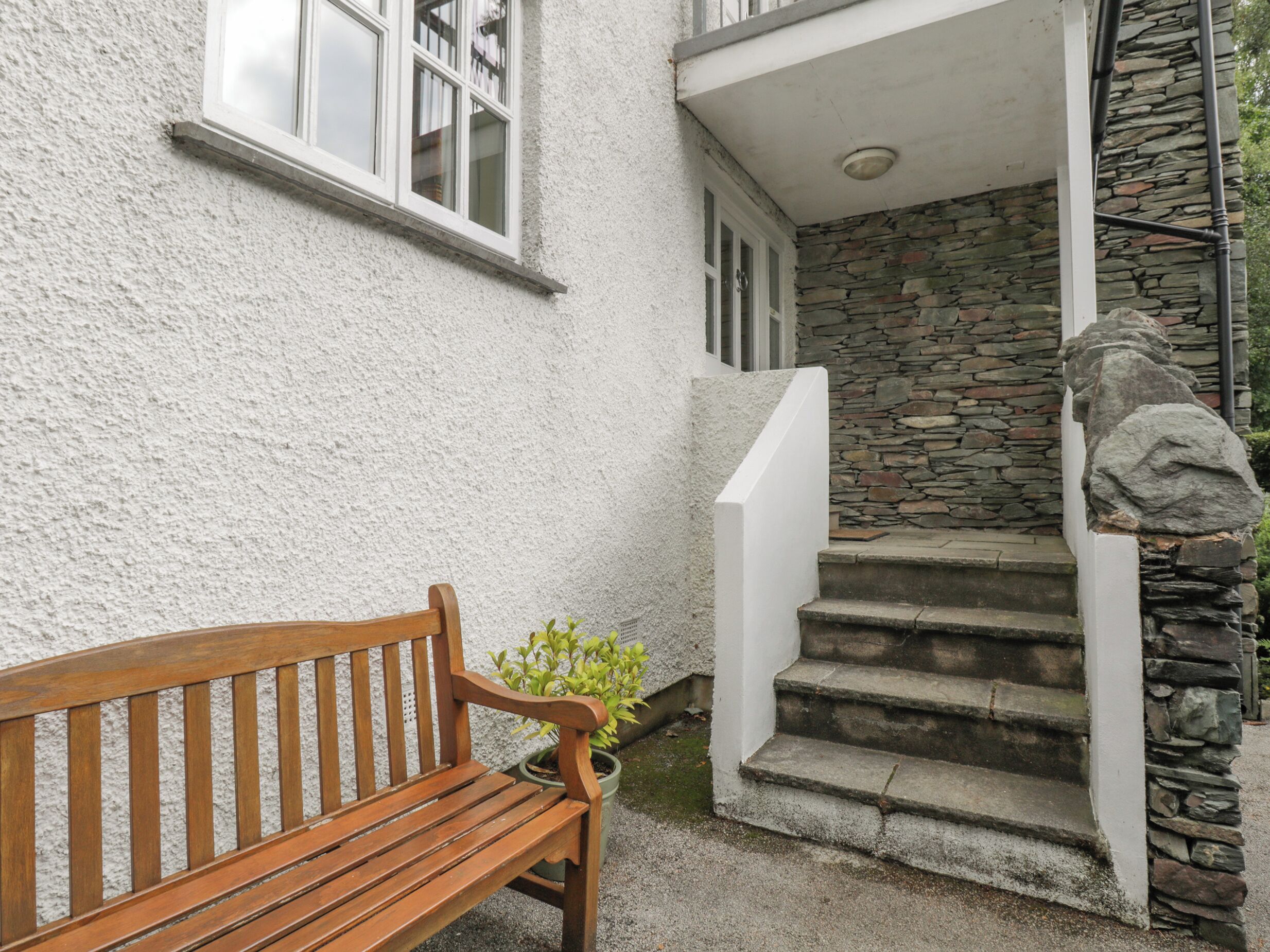 Un banc en bois se trouve à l’extérieur d’un bâtiment doté d’un escalier en pierre et d’un mur blanc.