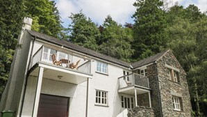 Uma casa de dois andares com fachada de pedra, garagem e varanda com móveis de exterior.