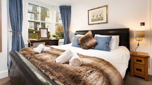 A neatly made bed with a brown furry blanket, a headboard, and a bedside table with a lamp. - Oak Cottage (Windermere)
