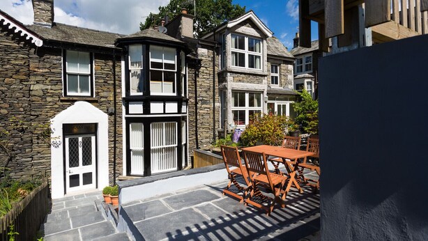 A stone cottage with a black and white exterior, a tiled patio, and a wooden table and chairs. - Oak Cottage (Windermere)