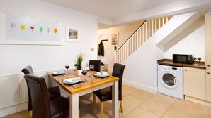 A dining area with a wooden table set for four, a washing machine, and a staircase leading to another room. - Oak Cottage (Windermere)
