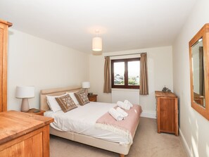 A bedroom with a bed, bedside lamps, a wooden nightstand, a wooden dresser, a window with curtains, and a mirror. - Garden House (Ambleside)