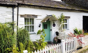 Una cabaña blanca con puerta verde, cerca de piquetes blancos y un letrero que dice "The Cottage".