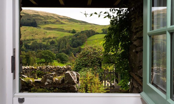 A view from a window overlooking a green valley with stone walls and a wooden fence.
