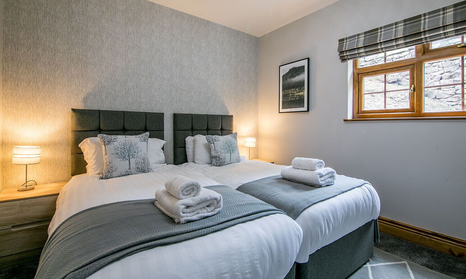 Une chambre d’hôtel avec un grand lit, deux tables de chevet, une fenêtre donnant sur un beau paysage et un tableau encadré au mur.