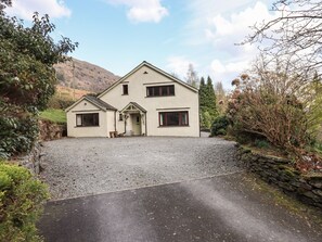 A two-story house with a gravel driveway and a stone wall.