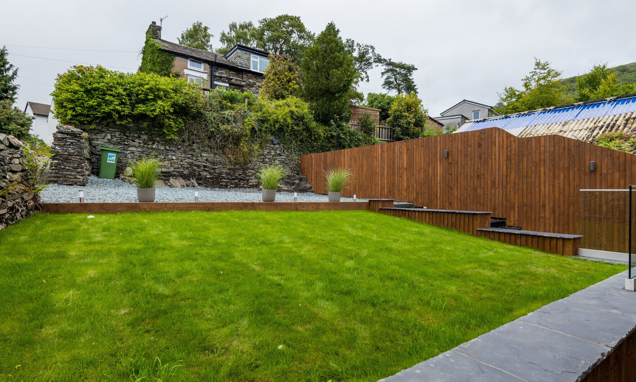 A well-maintained backyard with a grassy lawn, a stone wall, and a wooden fence.