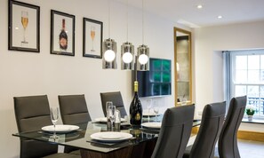 A modern dining area with a glass table, black chairs, and framed artwork on the wall. - Fisherbeck Farm Cottage (Ambleside)