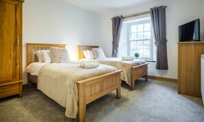 A bedroom with two wooden beds, a window with curtains, a television, and a wardrobe. - Fisherbeck Farm Cottage (Ambleside)