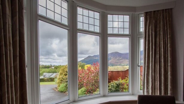A room with a bay window overlooking a garden and mountains. - Riggside (Keswick)