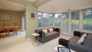 A modern living room with a grey sofa, a coffee table, and a dining area with a wooden table and chairs. - Riggside (Keswick)