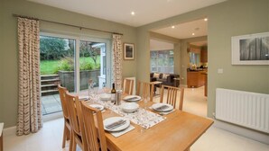 A dining area with a wooden table set for six, surrounded by chairs. There is a glass door leading to a garden. - Riggside (Keswick)