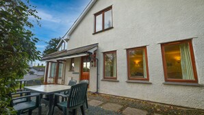 A white building with a patio area, including a table and chairs, and a covered seating area. - Holly Cottage (Ambleside)