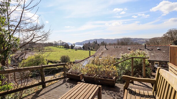 Una terraza de madera con bancos que da a un campo verde y colinas lejanas.