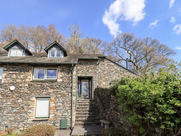 A stone house with a steeply pitched roof, a small front porch, and a staircase leading to the entrance. - Oak Bank (Windermere)