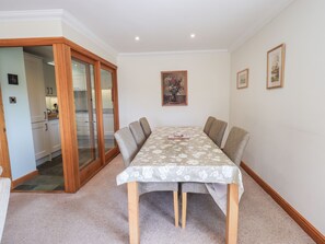A dining area with a table set for four, a kitchen visible through a glass door, and framed artwork on the wall. - Oak Bank (Windermere)