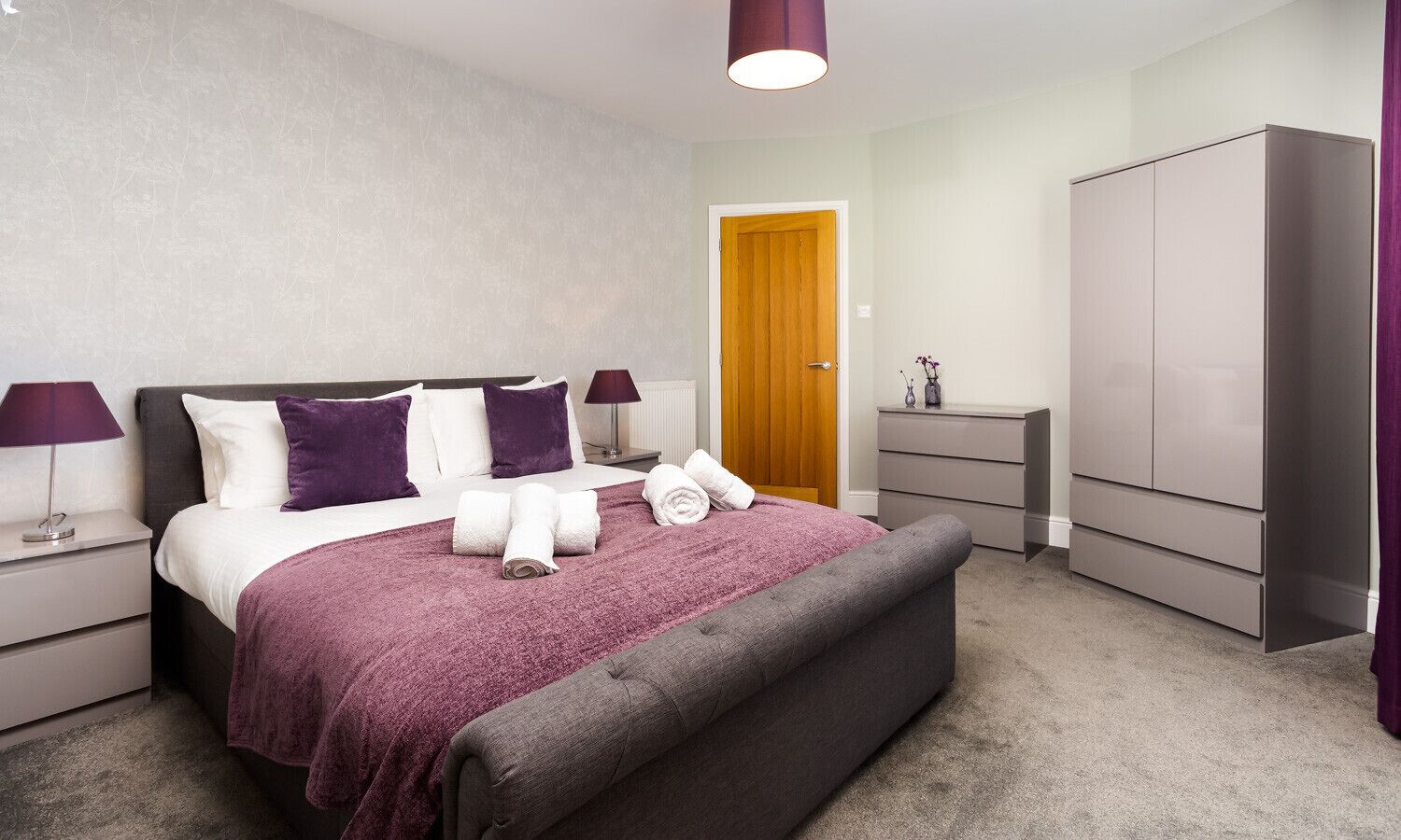 A modern bedroom with a bed, nightstands, a wardrobe, and a door.