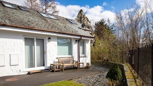Un bâtiment blanc avec un toit en pente, de grandes fenêtres et un banc à l’extérieur.