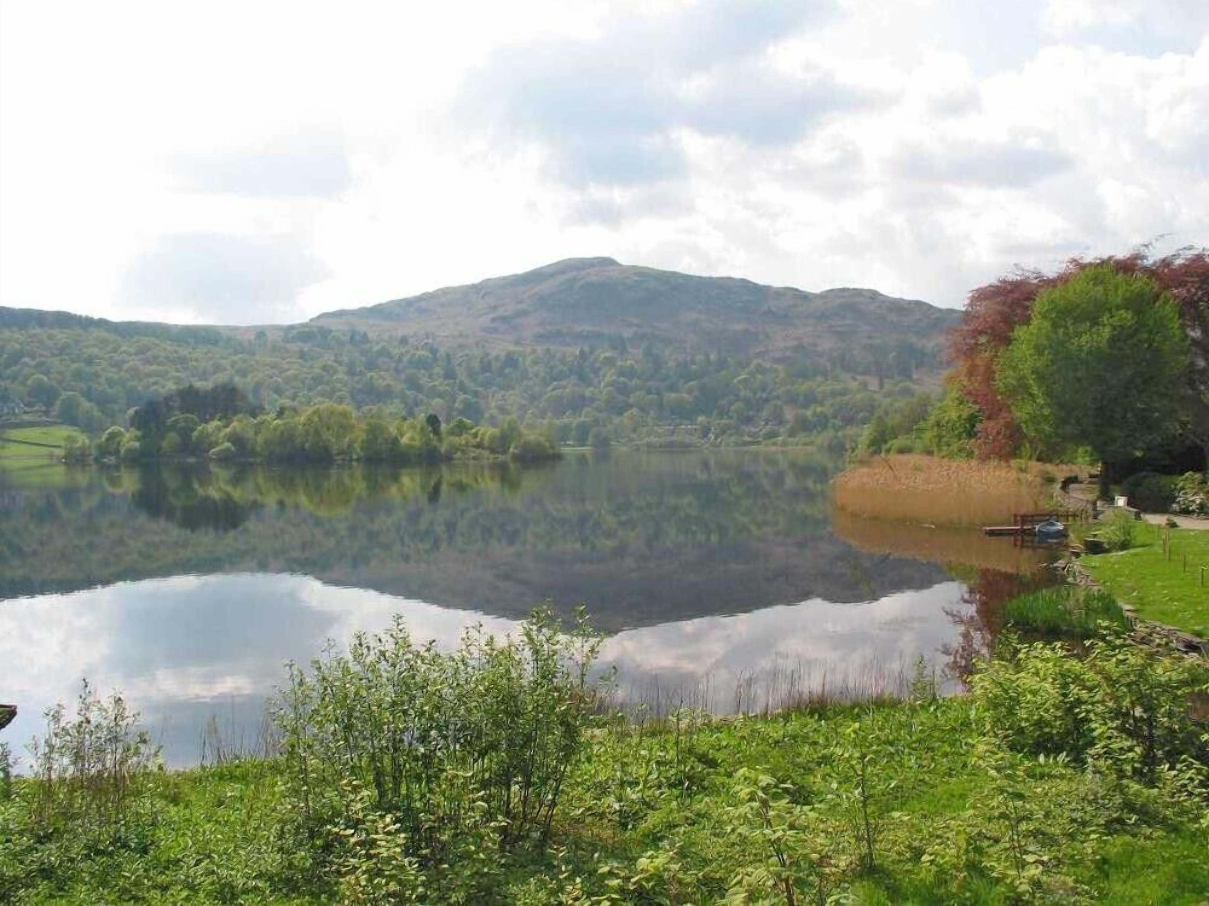 A serene lake with a clear reflection, surrounded by lush greenery and hills in the background.