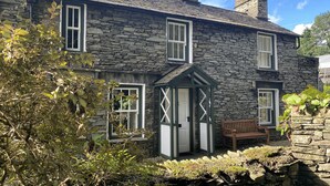 Una casa de piedra con varias ventanas, una pequeña puerta de madera y un banco en el patio.