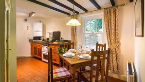 Una cocina con armarios de madera, una mesa de comedor para cuatro personas y una ventana con cortinas.