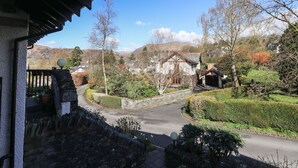 A traditional stone building with a wooden porch, surrounded by well-maintained hedges and trees. - The Spinney (Ambleside)
