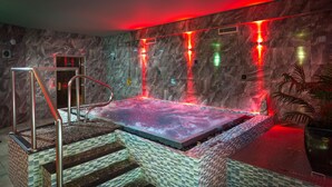 A hot tub with a tiled floor and metal railings, surrounded by stone walls and red lighting. - The Spinney (Ambleside)