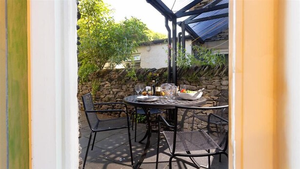 Une terrasse avec une table ronde et des chaises, un mur en pierre et de la verdure en arrière-plan.