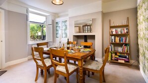 Une salle à manger avec une table en bois dressée pour six personnes, entourée de six chaises. Une bibliothèque se trouve sur le côté droit, contenant divers livres et objets décoratifs.