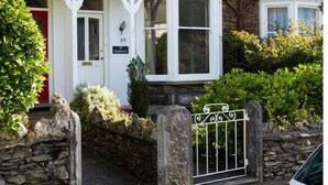 Une maison en pierre à deux étages, dotée d’un porche blanc et d’une entrée fermée par un portail.