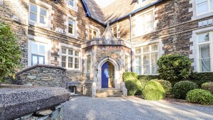 A stone building with a blue door, a gravel driveway, and well-maintained hedges. - Loughrigg Suite (Ambleside)