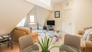 A spacious loft with a high ceiling, a TV, a dining area, and a cozy seating arrangement. - Loughrigg Suite (Ambleside)