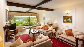 A spacious living room with a large window offering a scenic view, a fireplace, and a cozy seating area with multiple sofas and a coffee table.