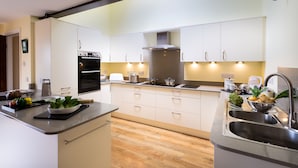 A modern kitchen with white cabinets, a built-in oven, a stainless steel sink, and a wooden floor.