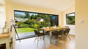 A dining area with a table set for four, large sliding glass doors leading to a garden, and a modern kitchen with a built-in oven. - Greengarth (Keswick)