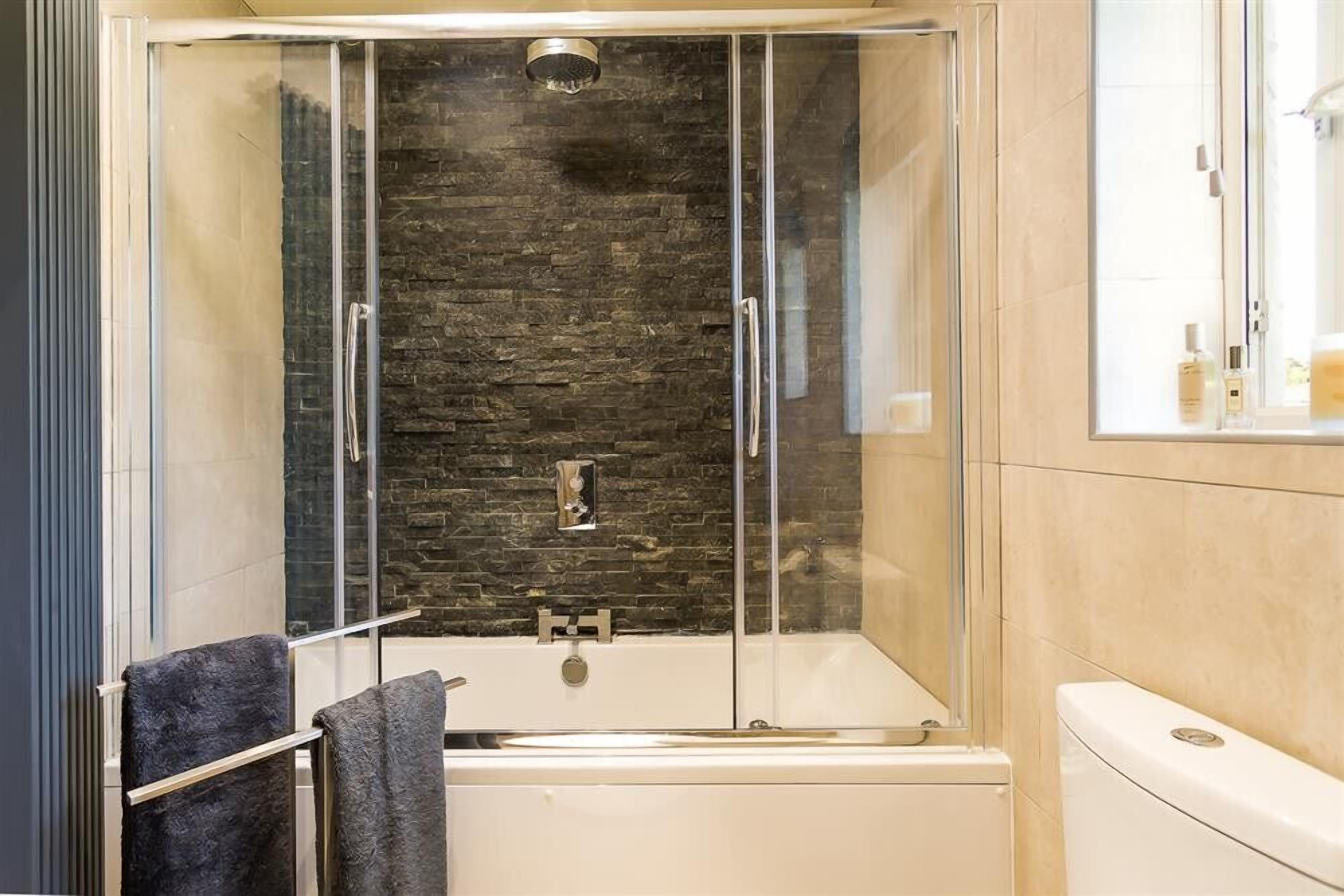A modern bathroom with a glass-enclosed shower, a white bathtub, and a toilet.