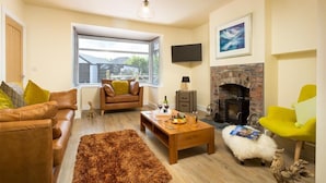 A living room with a sofa, a coffee table, a fireplace, and a window with blinds. - Greengarth (Keswick)