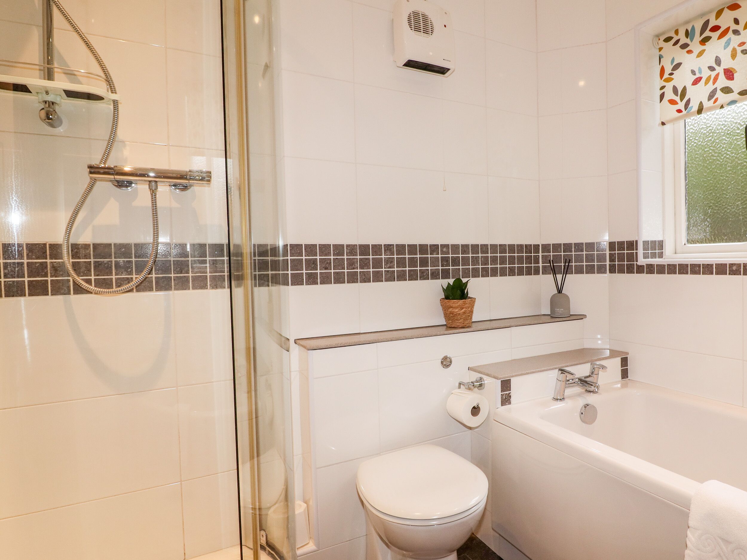 A modern bathroom with a glass shower enclosure, a white toilet, a bathtub, and a small shelf with a potted plant.