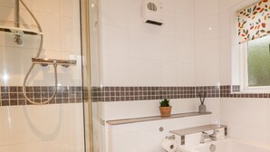 Un baño moderno con cabina de ducha de vidrio, un inodoro blanco, una bañera y un pequeño estante con una planta en maceta.